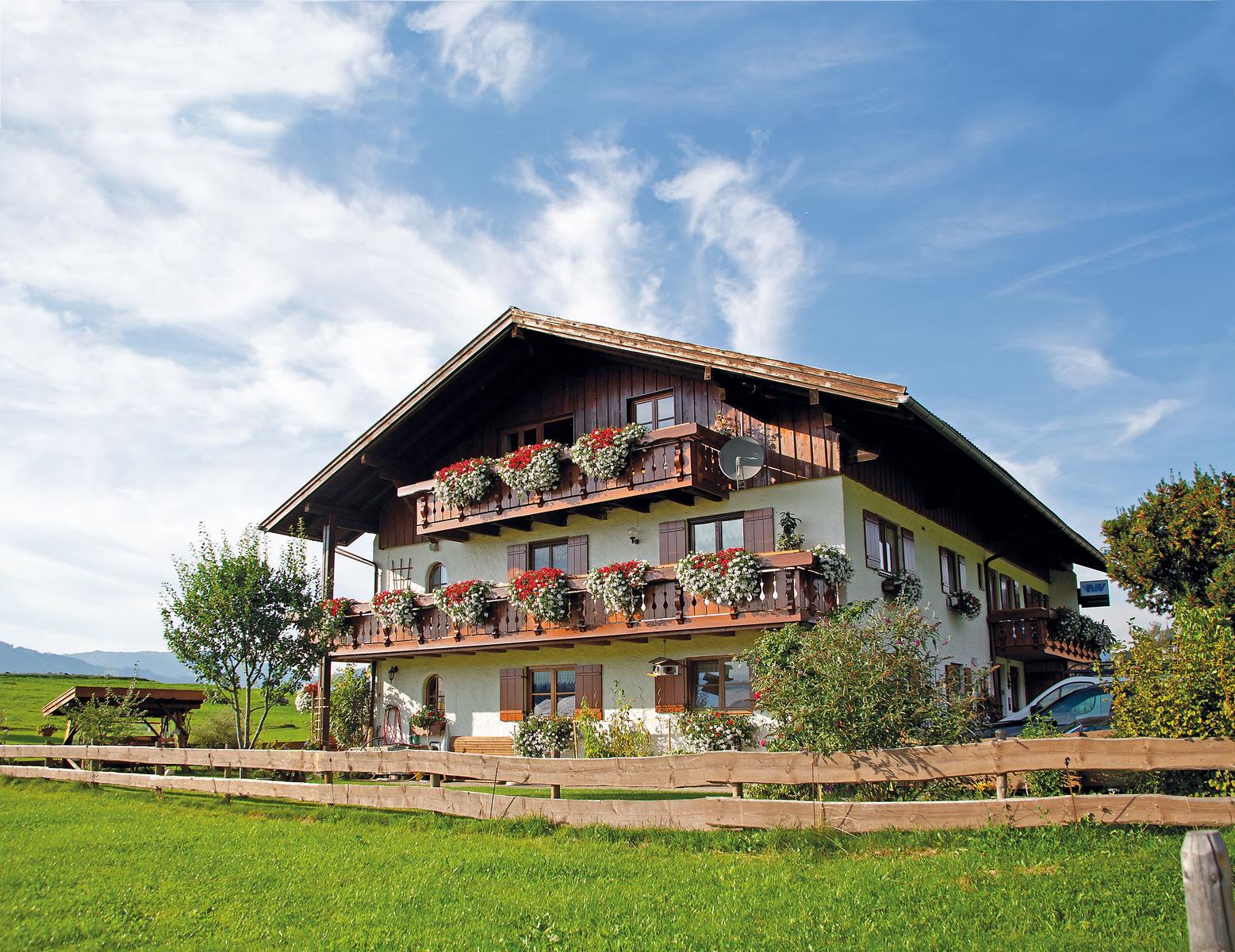Ein zweistöckiges Haus mit Balkonen, Blumen und grünem Grundstück unter blauem Himmel.