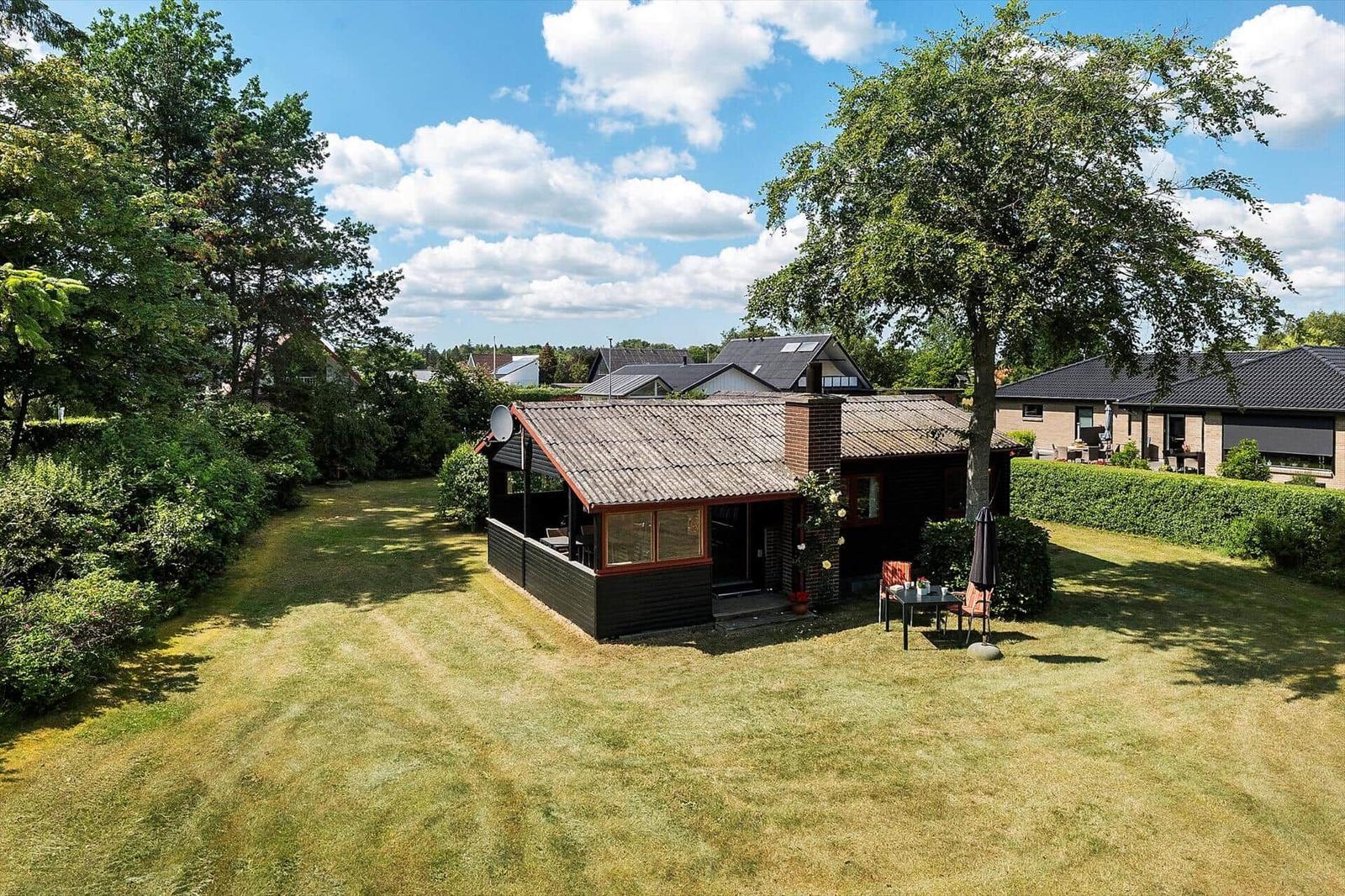 Schwarzes Holzhaus mit Terrasse und Garten. Roter Rahmen an Fenstern. Hinterhof mit Sitzgelegenheit.