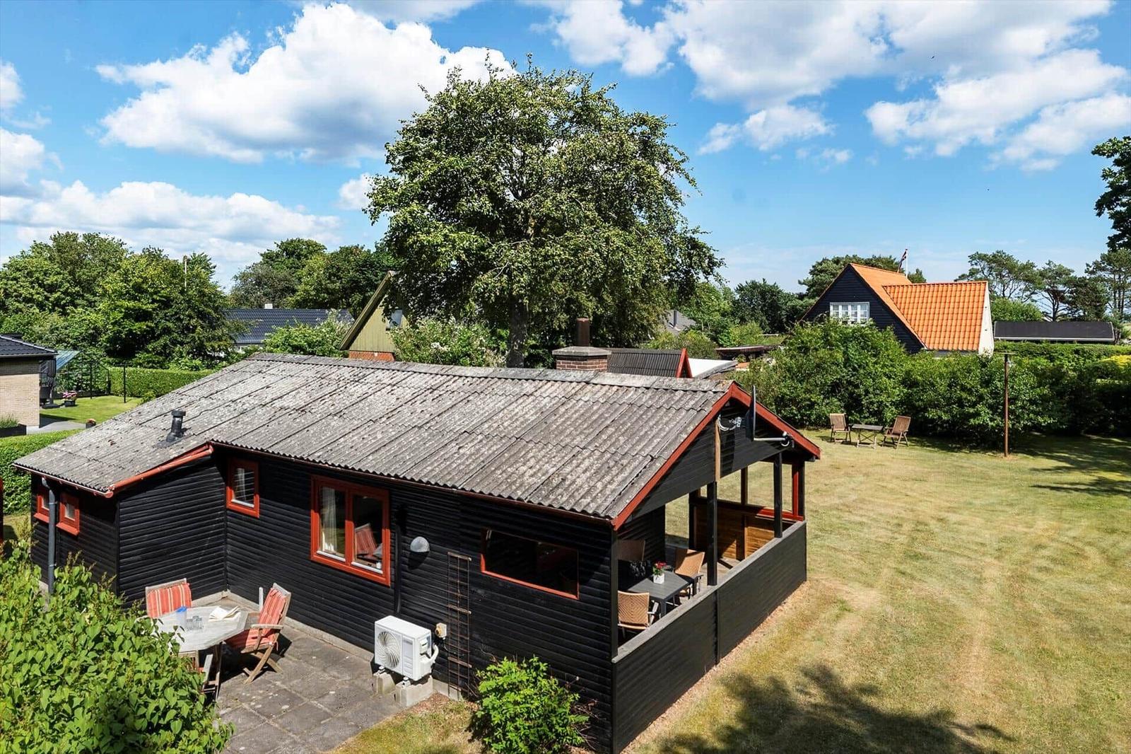 Holzhaus mit Grillplatz und Garten unter großen Baum.