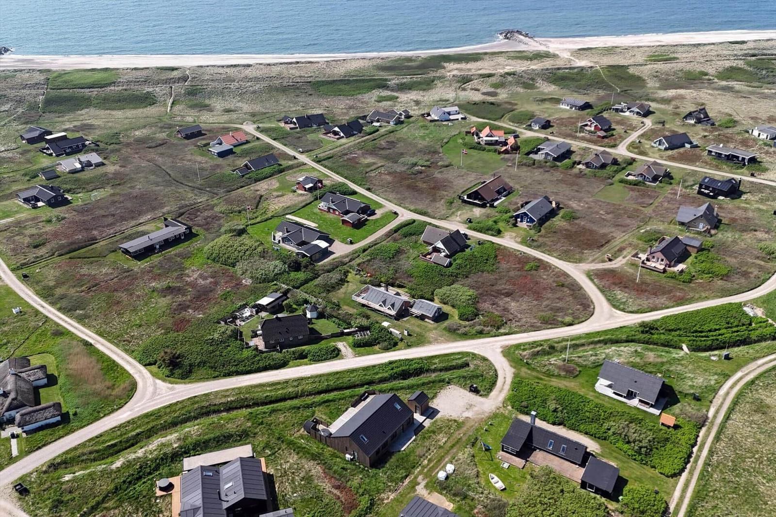 Aerial view of coastal village with scattered houses and winding dirt roads near the sea.
