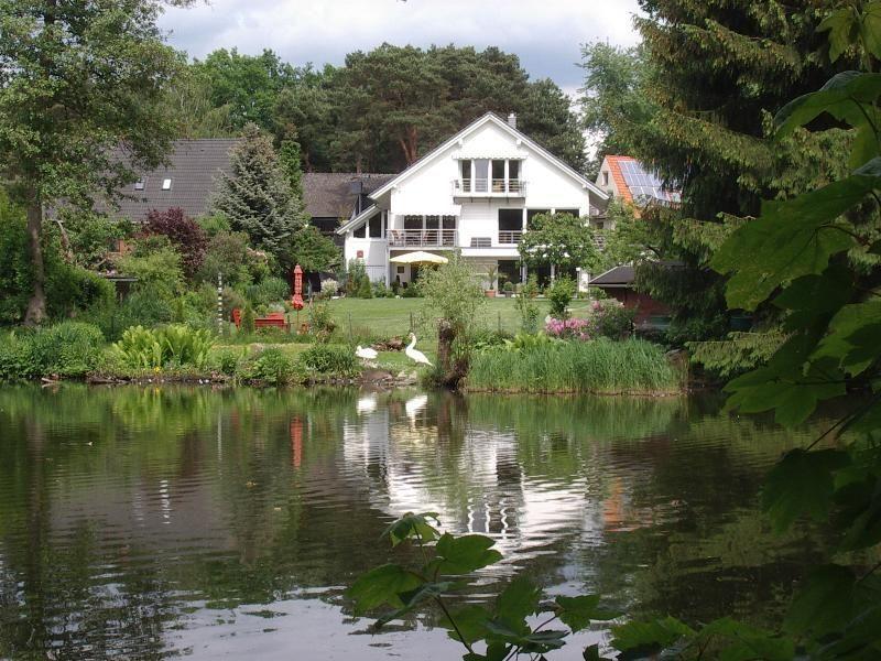 Ein weißes Haus mit Balkon steht am Ufer eines Sees. Weiße Schwäne schwimmen im Wasser.