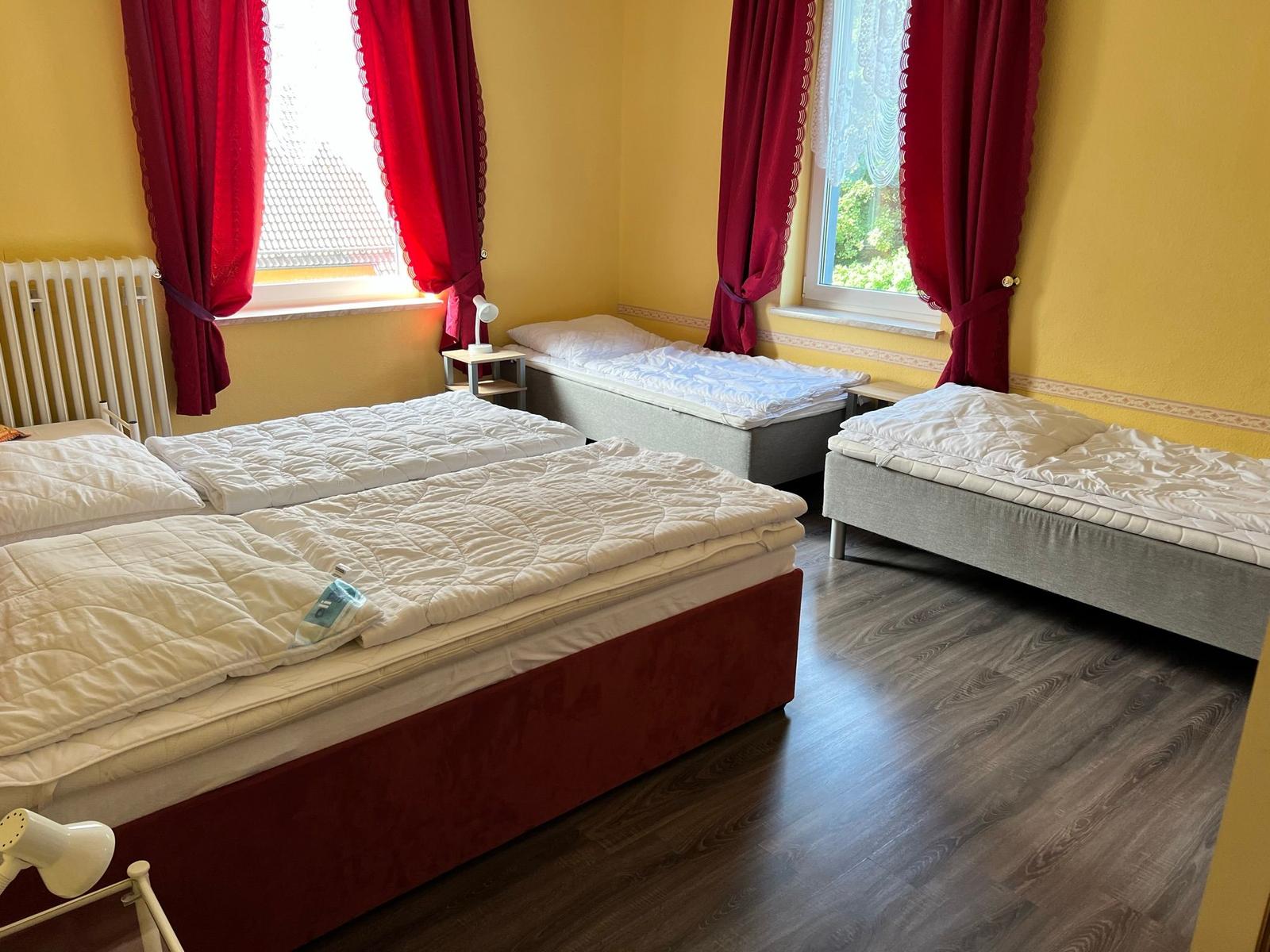 Zimmer mit drei Betten, gelben Wänden und roten Vorhängen.