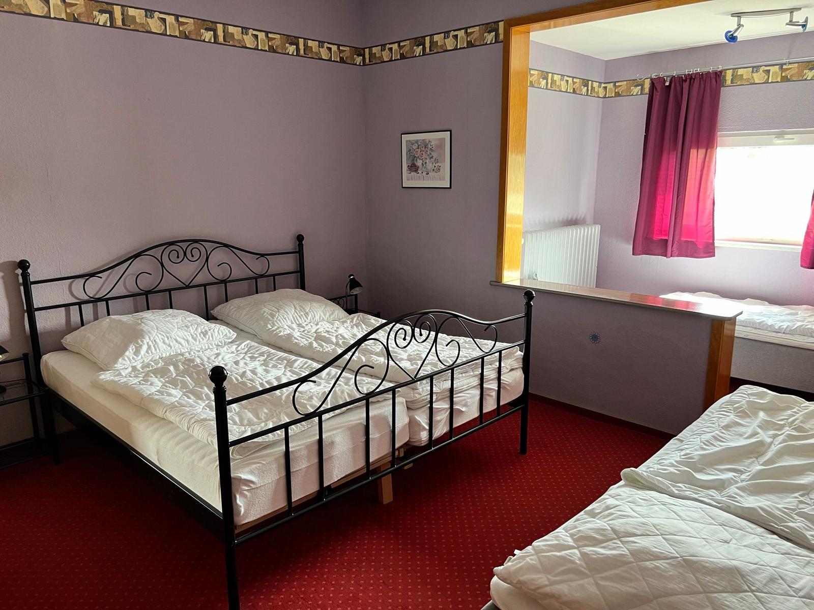 Zimmer mit zwei Betten, lila Wänden und rotem Teppichboden.