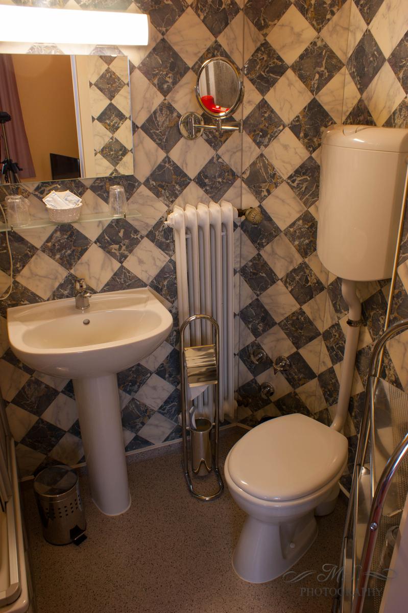 Badezimmer mit Waschbecken, Toilette und Spiegel an schwarz-weiß gemasertem Wandverkleidung.