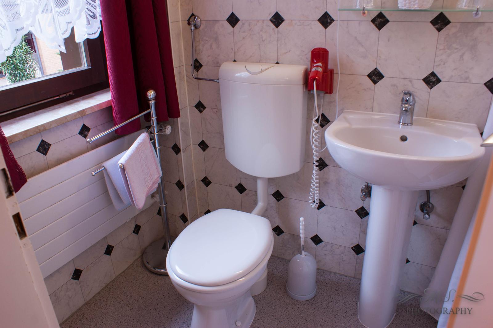 Badezimmer mit Toilette, Waschbecken und Fenster mit rotem Vorhang.