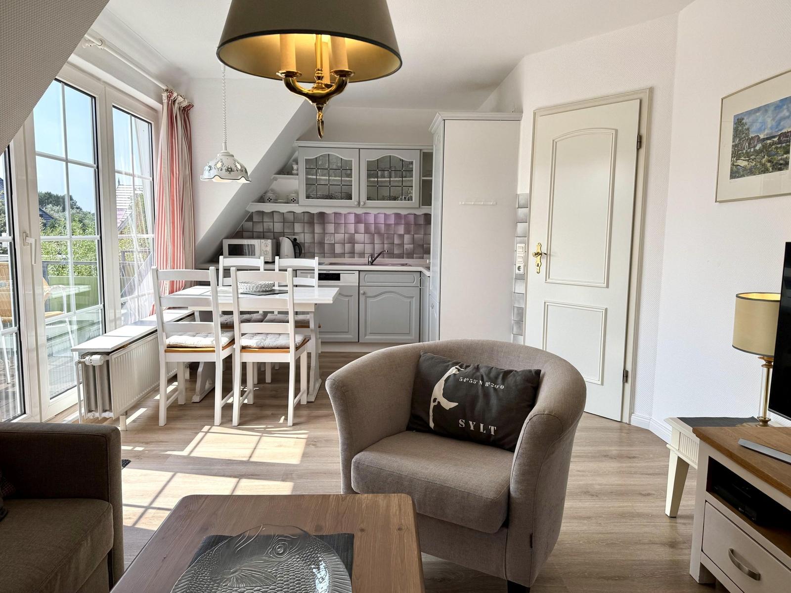 Living area with grey armchair, wooden table, dining area and kitchenette