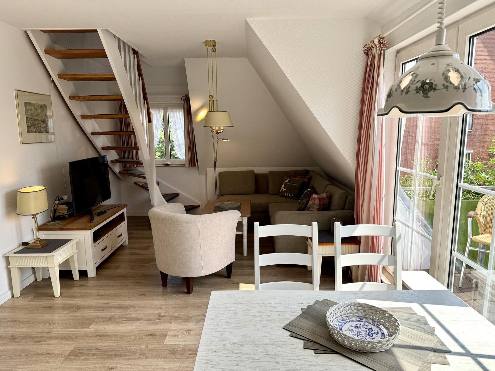 Bright living area with sofa under a slope, TV, wooden stairs and dining table