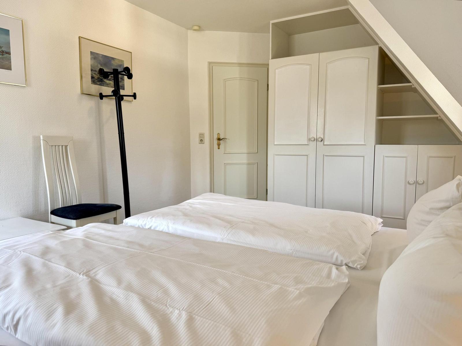 Bright bedroom with double bed, white built-in wardrobe and chair