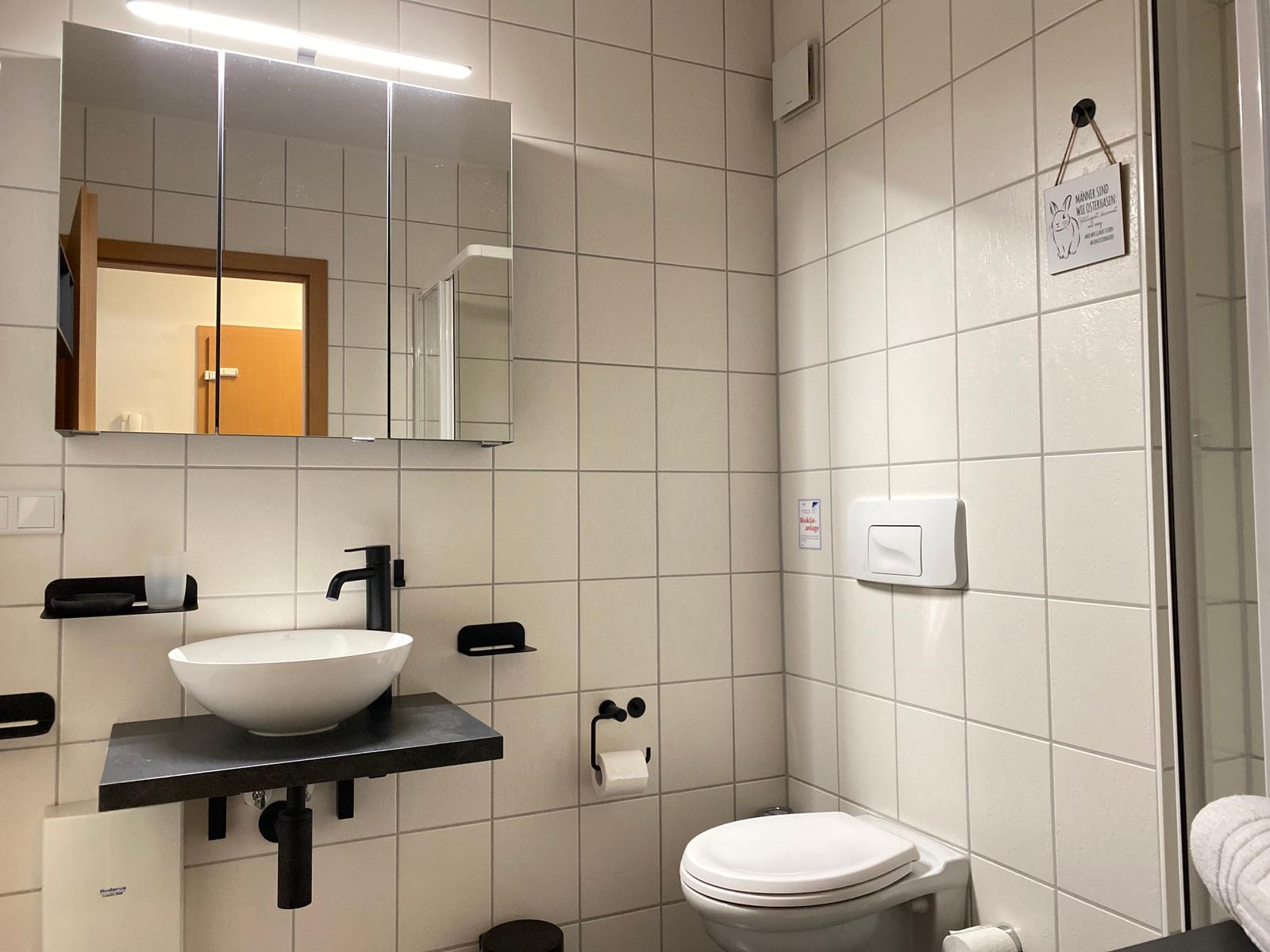Bathroom with sink, mirror, and toilet. White tiles and black fixtures.