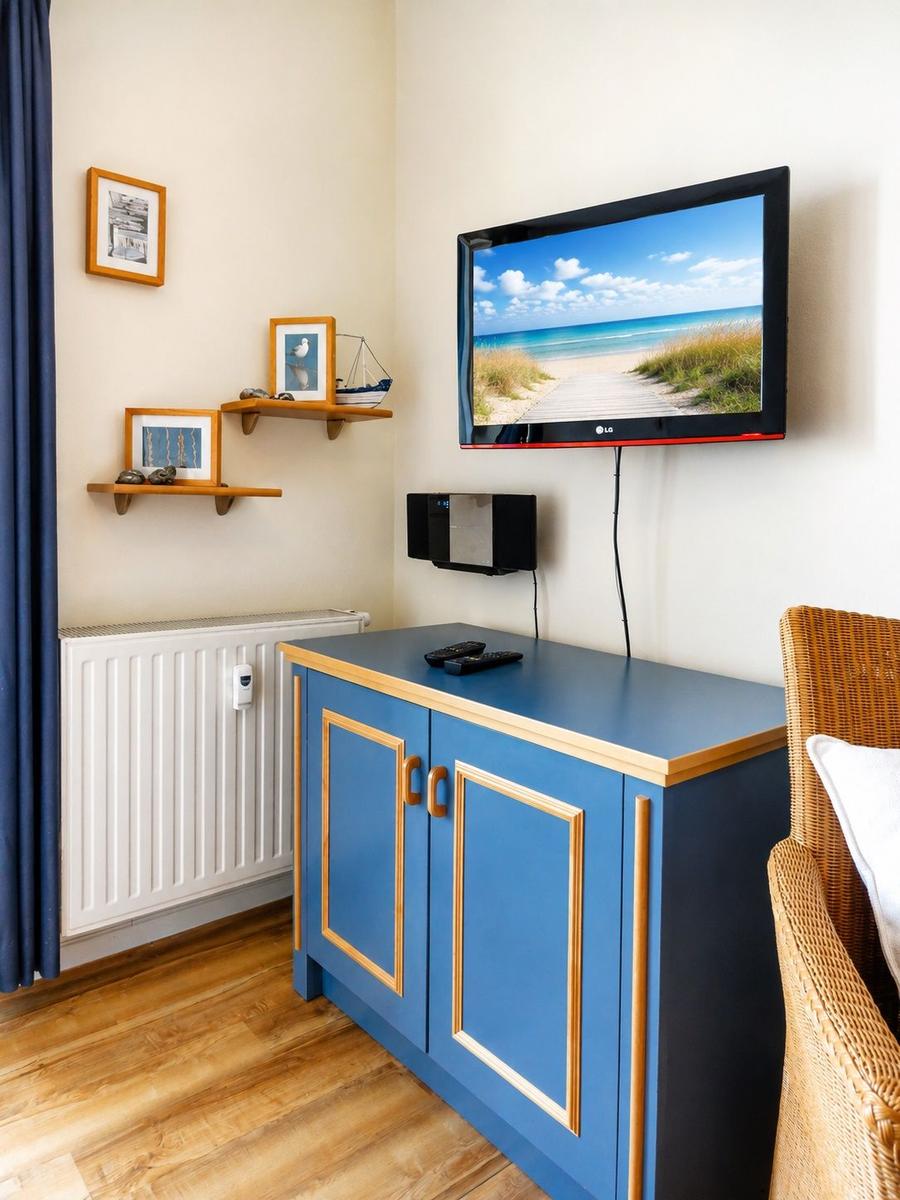 A room with blue cabinet, wall-mounted TV, and wooden floor. Pictures and shelves are on the wall.