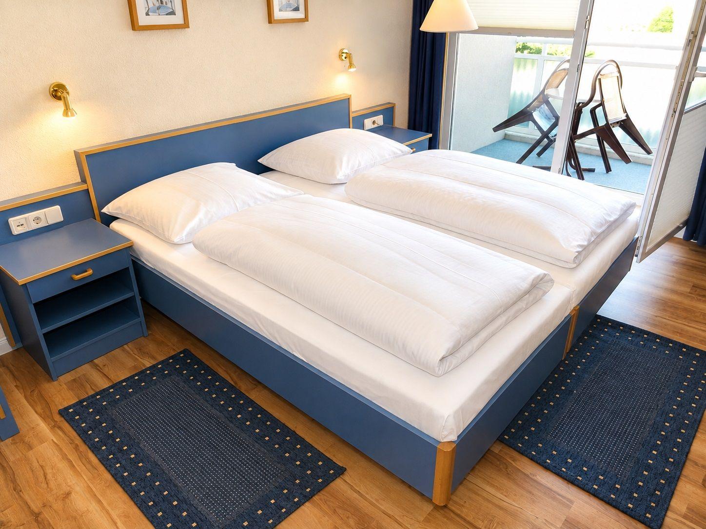 Double bed with white bedding, two nightstands, and balcony with chairs.