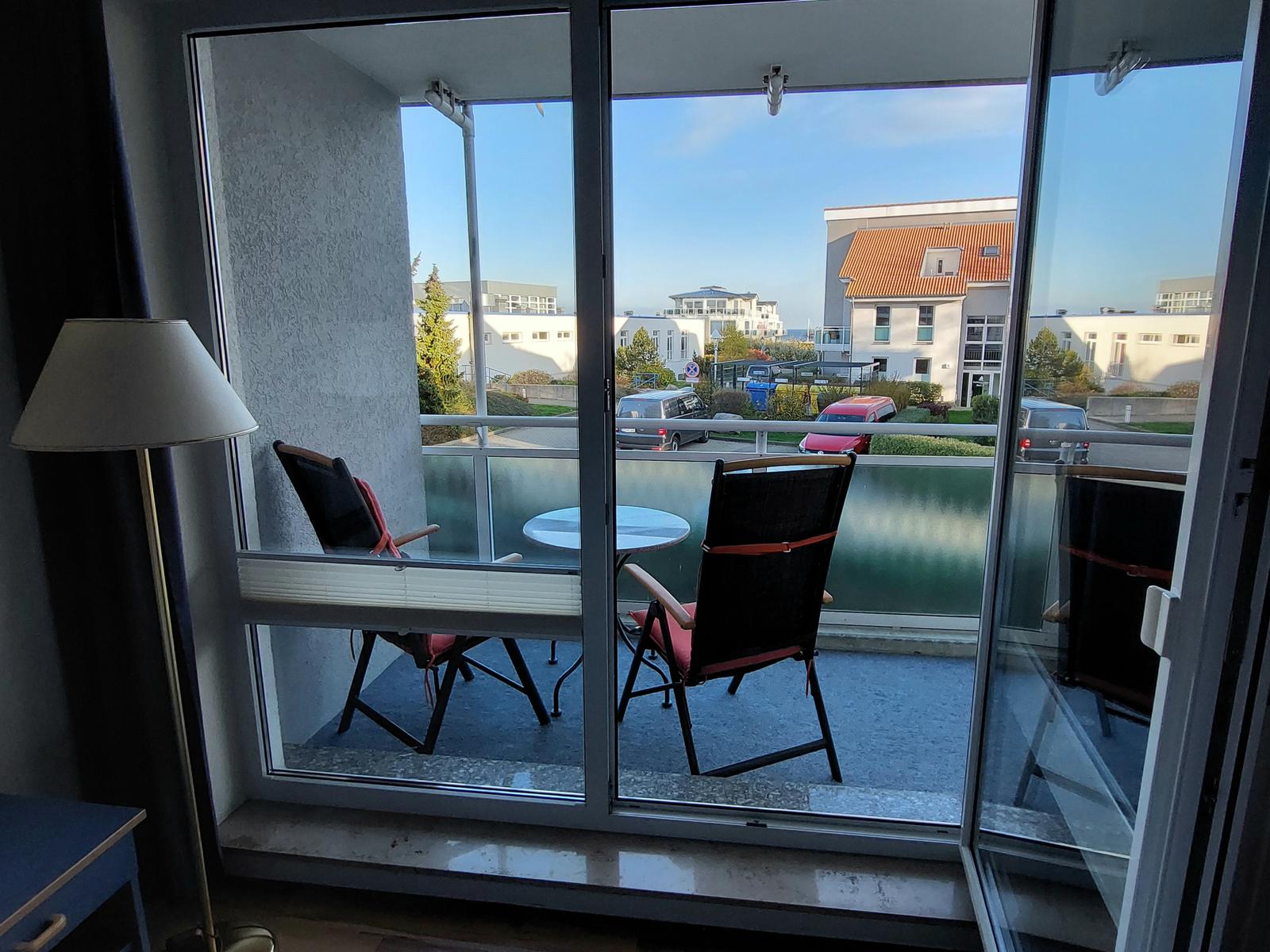 Balcony with table and two chairs, view of buildings and street.