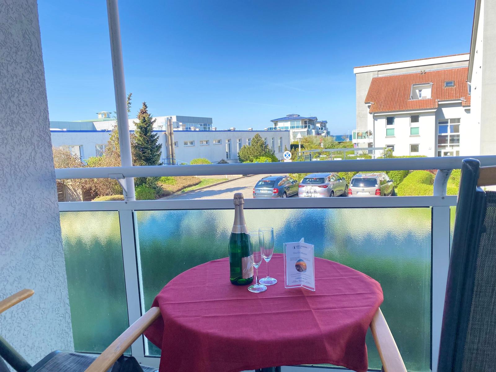 Balcony with table, champagne, and view of buildings and parking lot.
