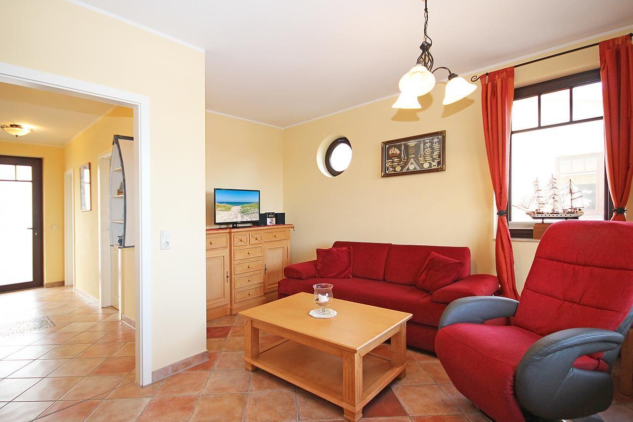 Wohnzimmer mit rotem Sofa, Holztisch und Fernseher. Fenster mit roten Vorhängen.