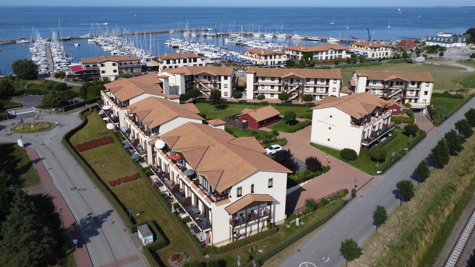 Meerfrontanlage mit mehreren Gebäuden, Terrassen und Bootshafen im Hintergrund.