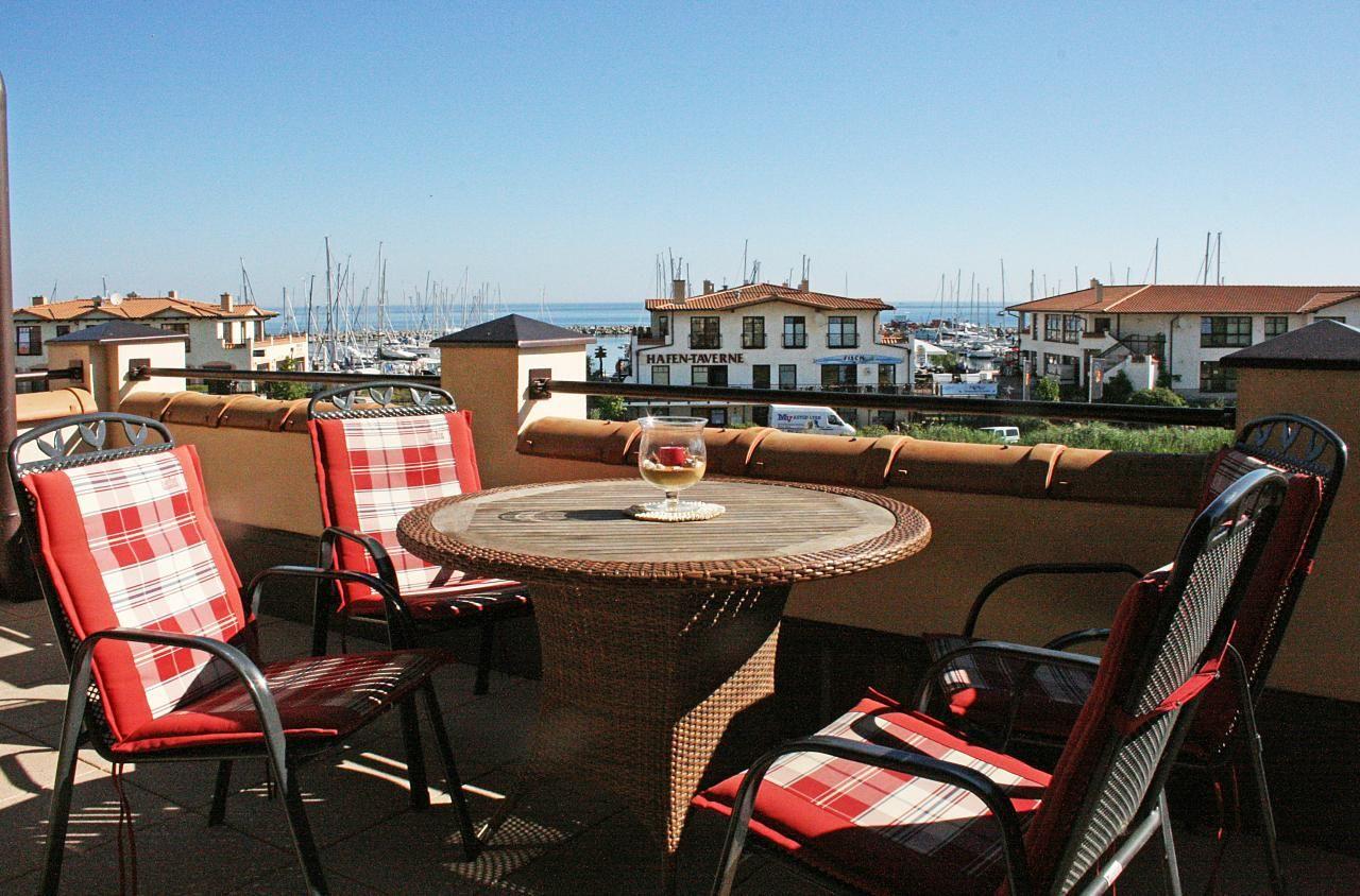 Terrasse mit Tisch und Stühlen, Blick auf Hafen und Meer.