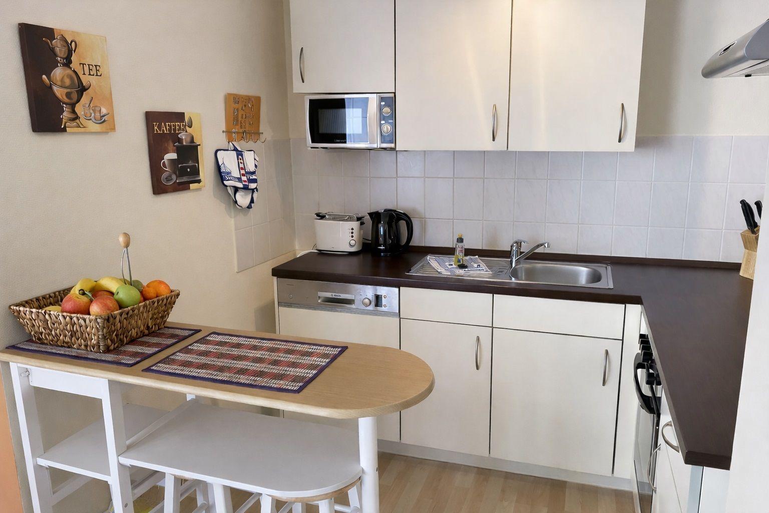 Küche mit Arbeitsplatte, Spüle, Mikrowelle und Essbereich mit Tisch und Stühlen.