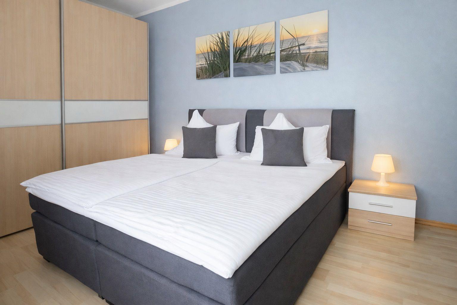 Schlafzimmer mit Doppelbett, Nachttisch und Kleiderschrank. Wandbild zeigt Strand.