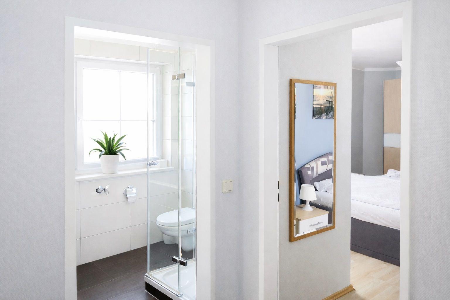 Badezimmer mit Dusche und Toilette. Schlafzimmer mit Bett und Spiegel.