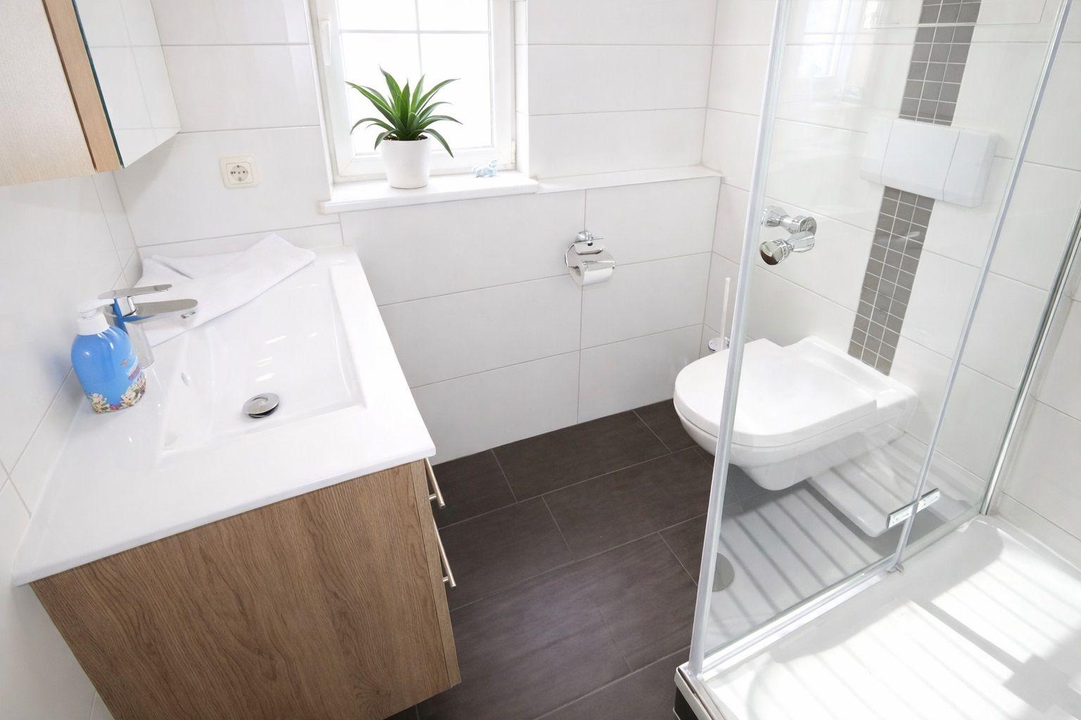 Badezimmer mit Waschbecken, Toilette und Dusche. Fenster mit Pflanze.