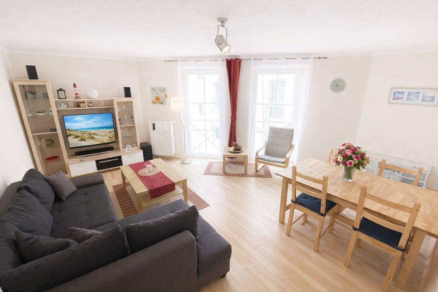 Wohn- und Essbereich mit Sofa, TV, Esstisch und Fenstern.