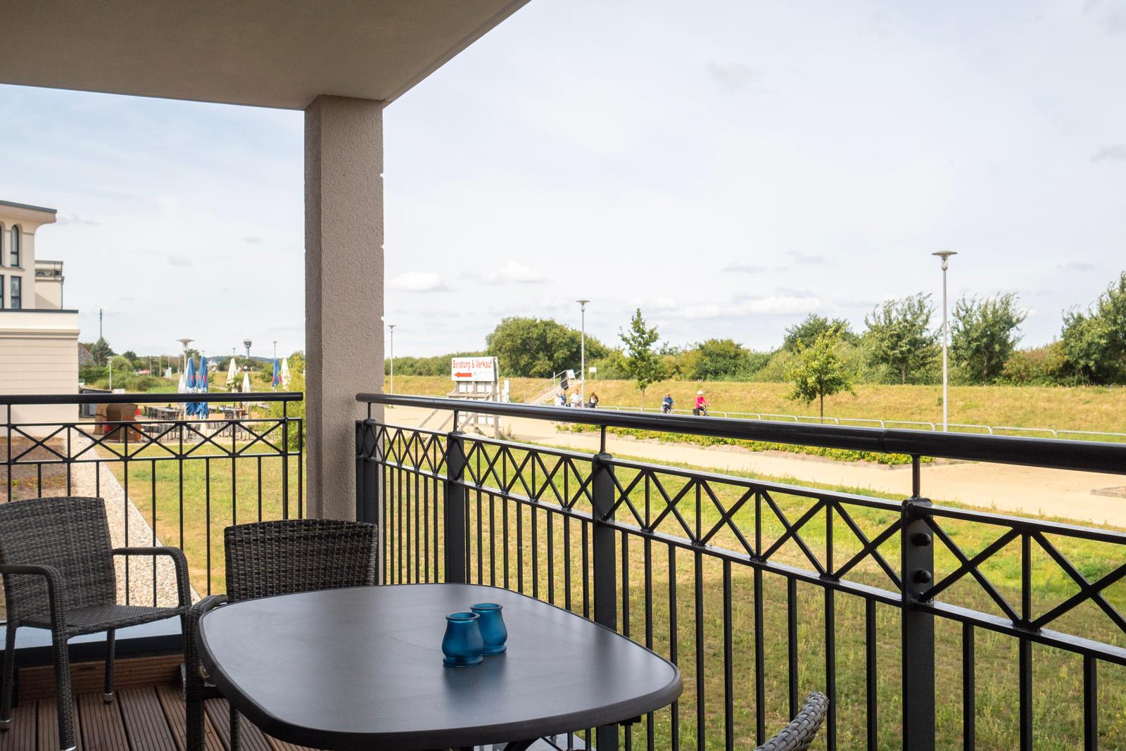 Terrasse mit Tisch und Stühlen, Blick auf Grünfläche und Weg.
