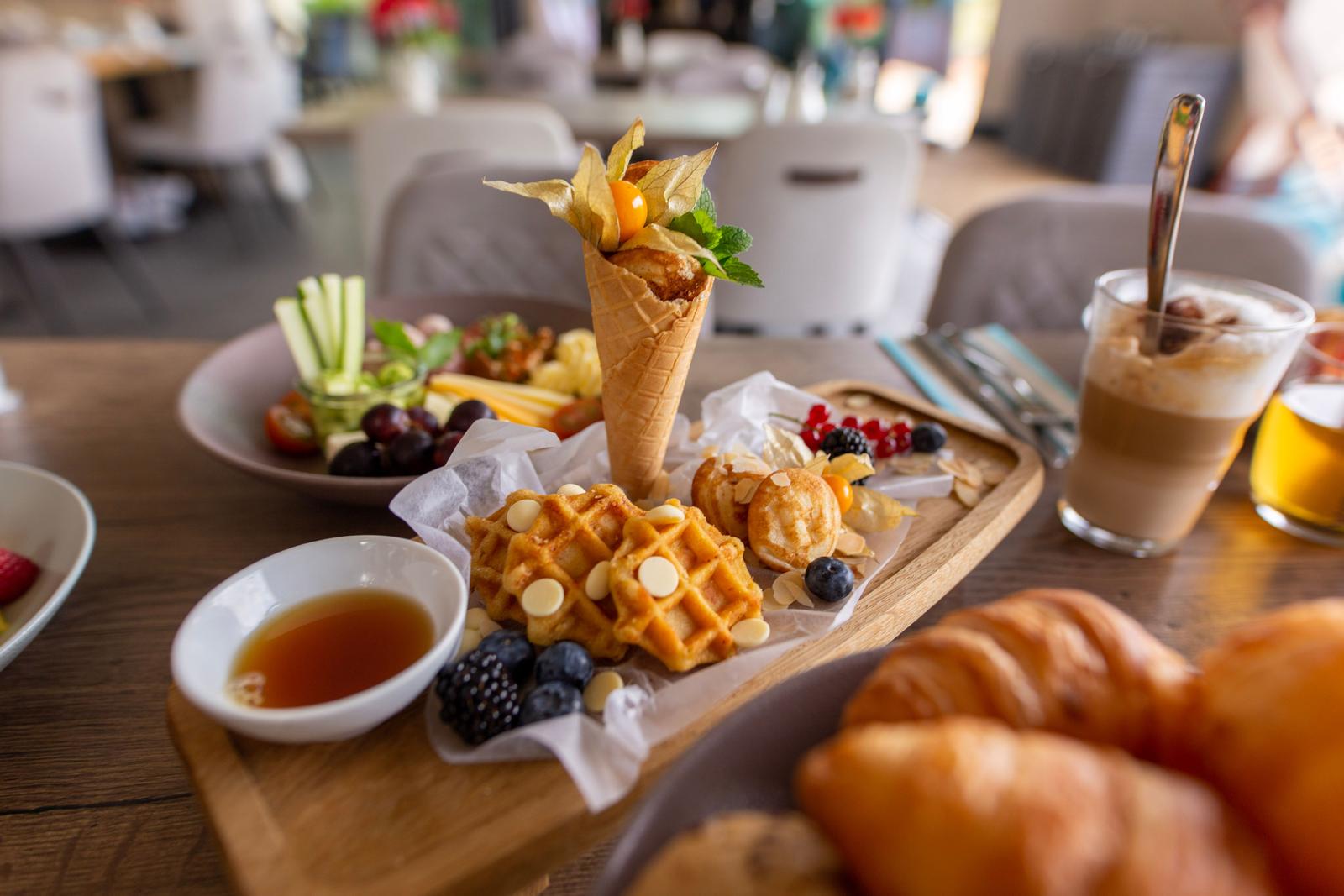 Frühstückstablett mit Waffeln, Obst und Getränken auf Holzbrett.