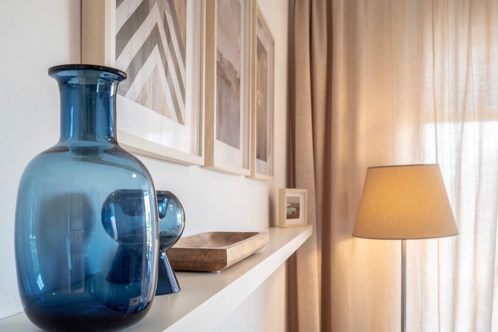 Regal mit blauem Vasen, Bildern und Lampe vor Vorhang