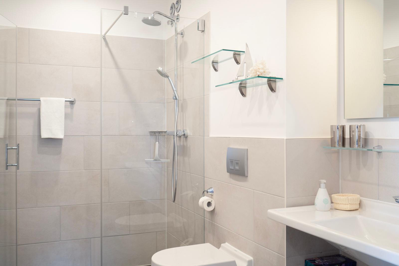 Dusche mit Glaswand, Waschbecken und Toilette in moderner Ausstattung.