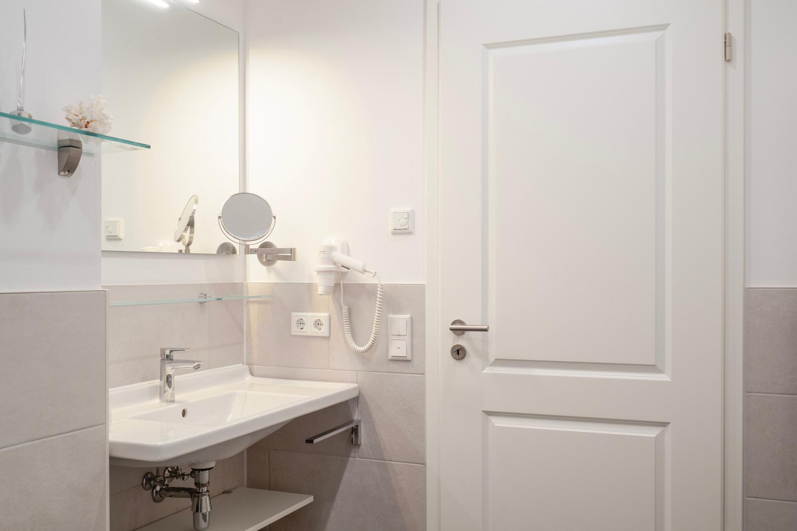 Badezimmer mit Waschbecken, Spiegel und Handtuchhalter.