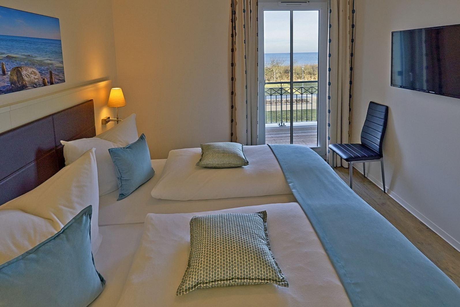 Schlafzimmer mit Blick aufs Meer, Bett, TV und Stuhl.
