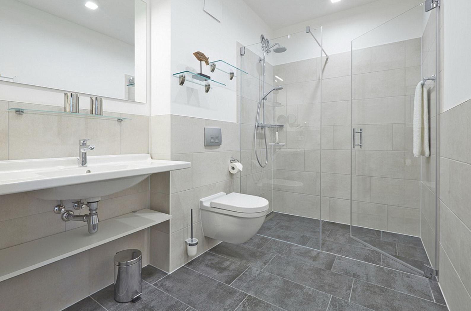 Badezimmer mit Dusche, Waschbecken und WC. Fliesenboden und Spiegelschrank.