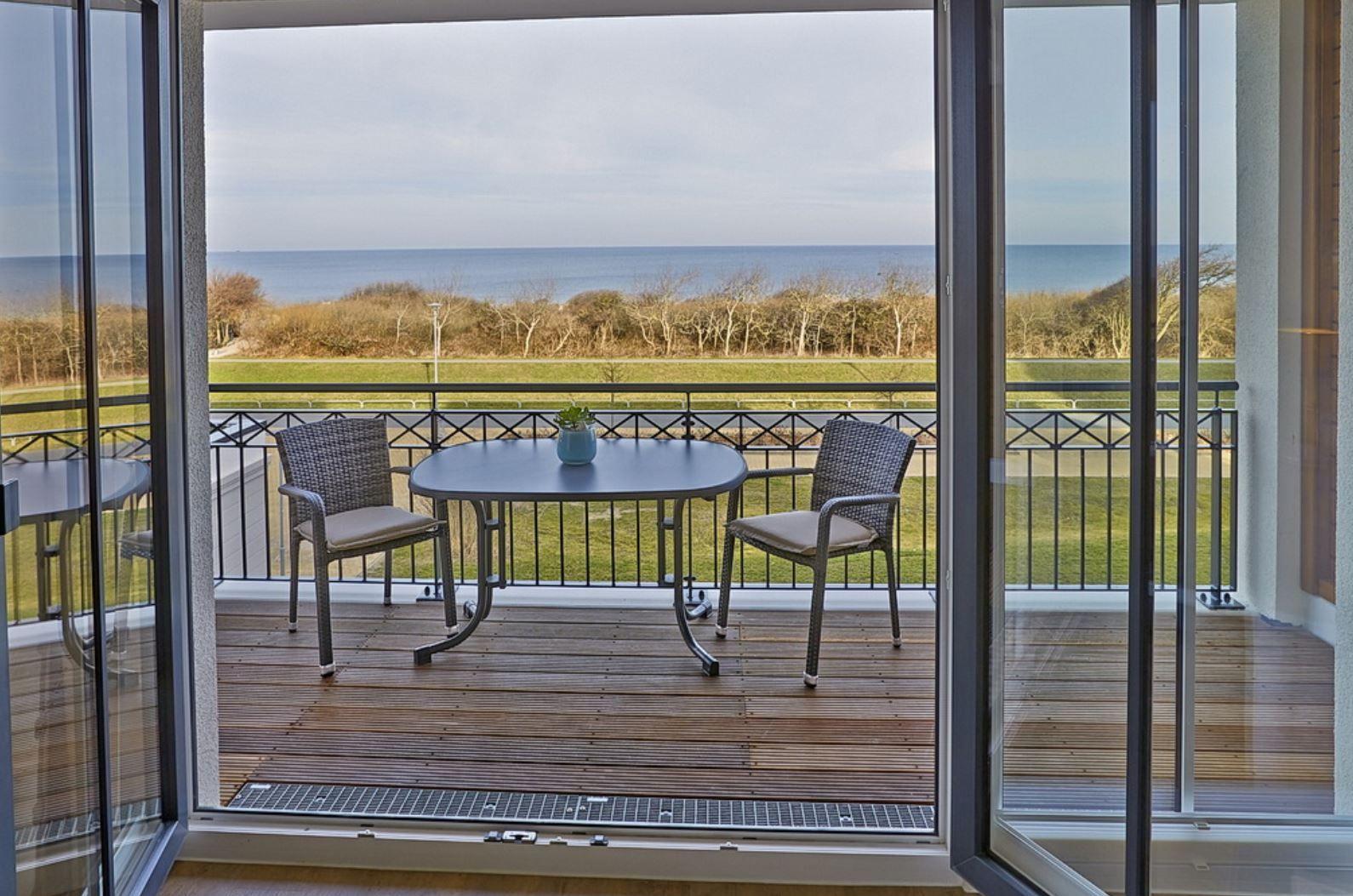 Terrasse mit Tisch und zwei Stühlen, Blick auf Meer und Grünfläche.