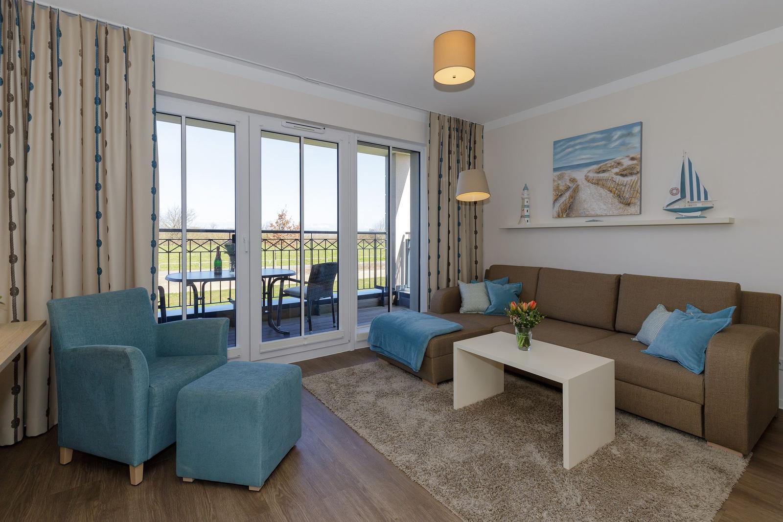 Wohnzimmer mit Sofa, Sessel und Balkonansicht.