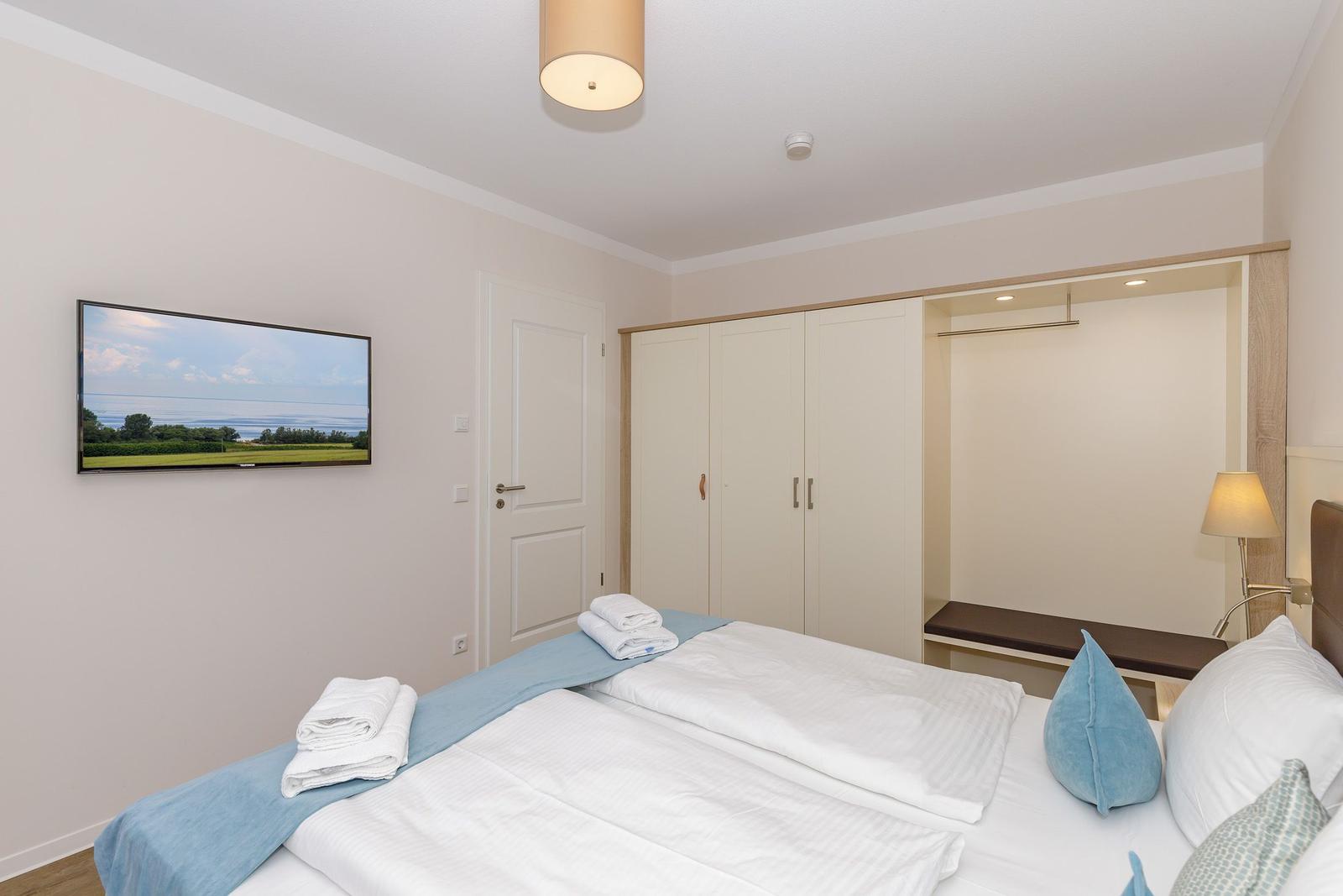 Schlafzimmer mit Doppelbett, Kleiderschrank und Fernseher an der Wand.