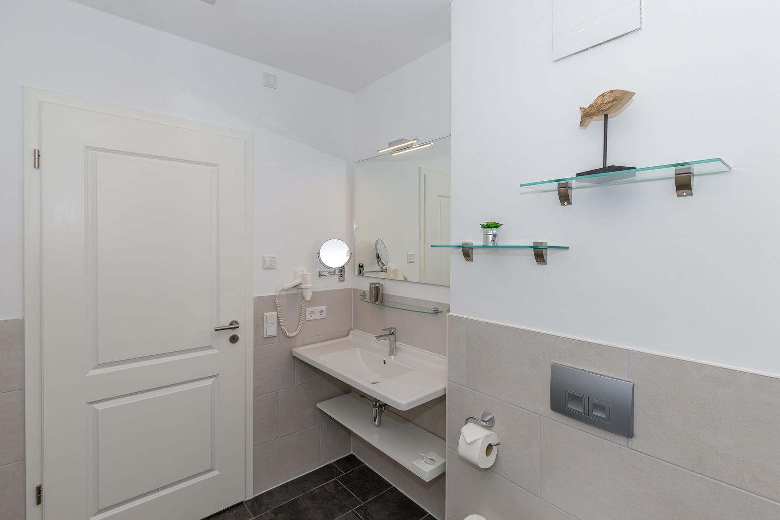Badezimmer mit Waschbecken, Spiegel und Glasregalen an der Wand.