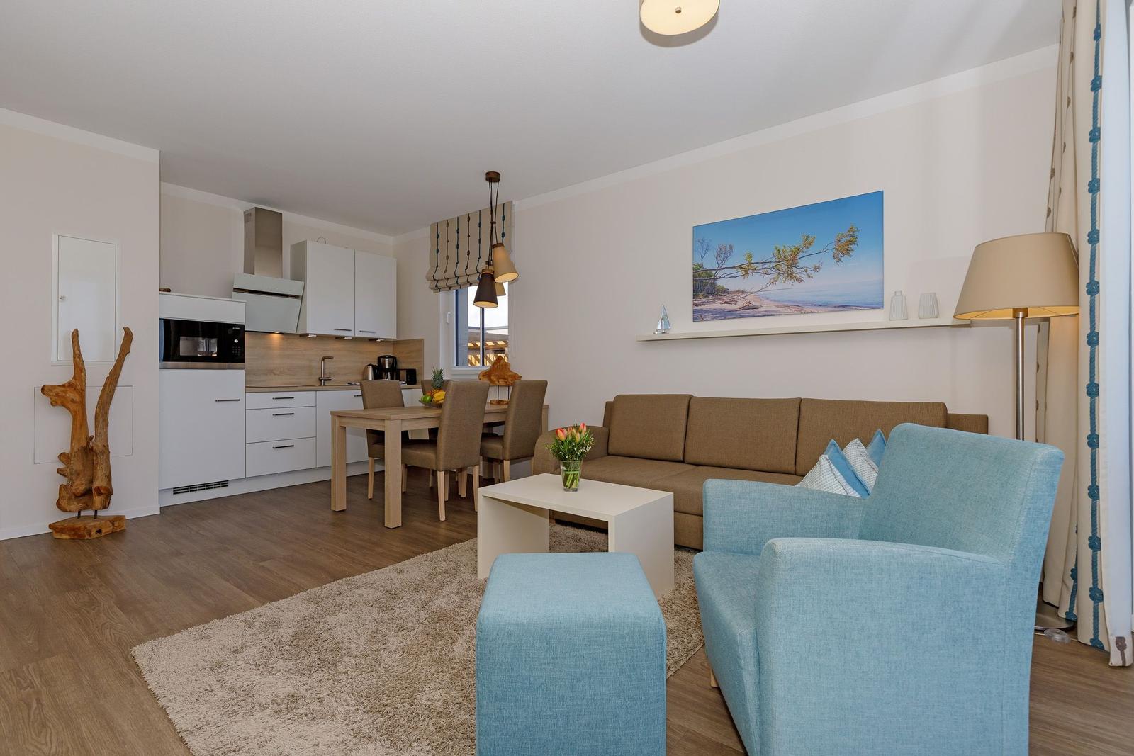 Wohnbereich mit Sofa, Sessel, Esstisch und Küche im Hintergrund.