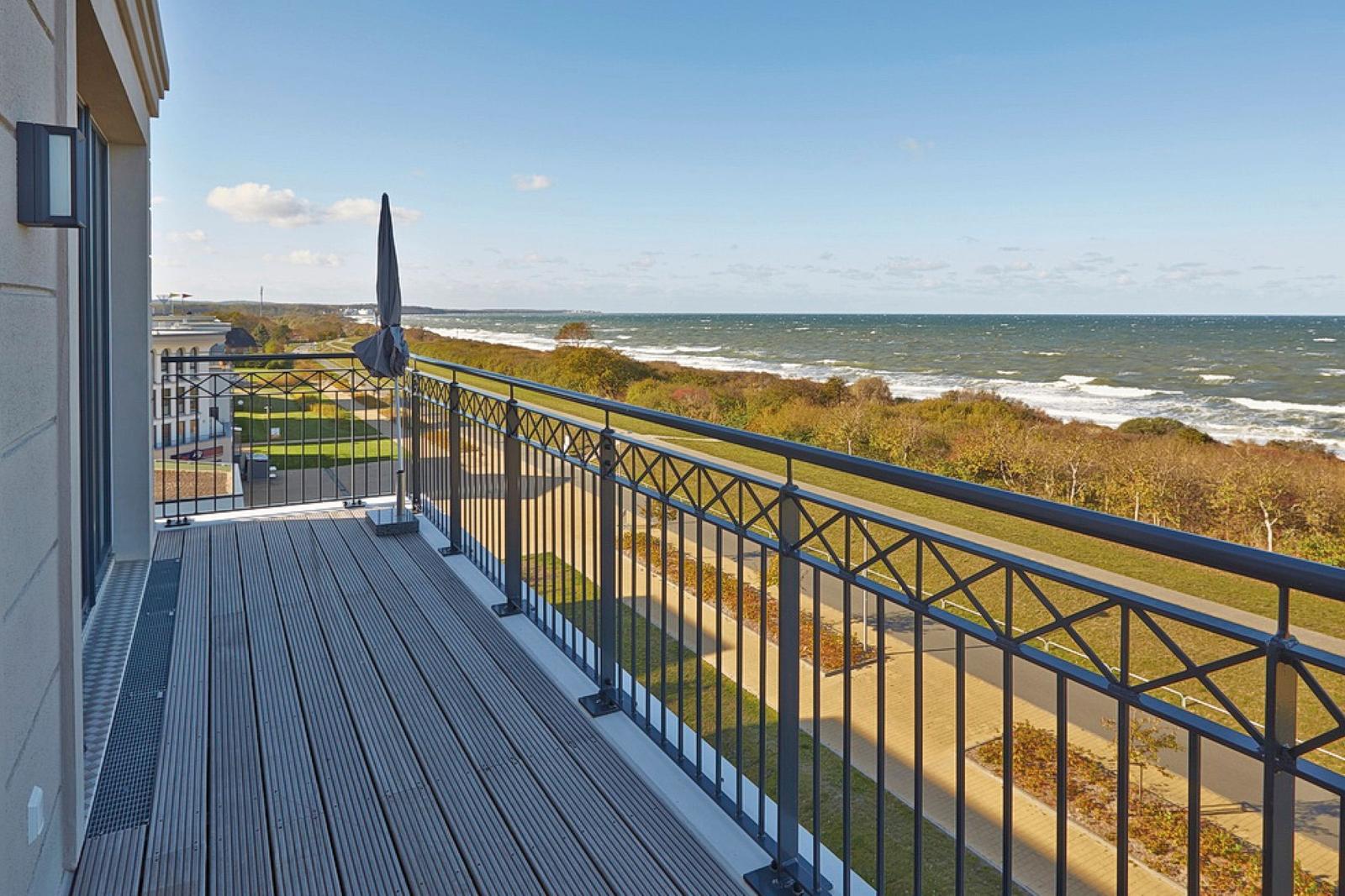 Terrasse mit Blick auf Meer und Strand. Metallgeländer und Sonnenschirm sind vorhanden.
