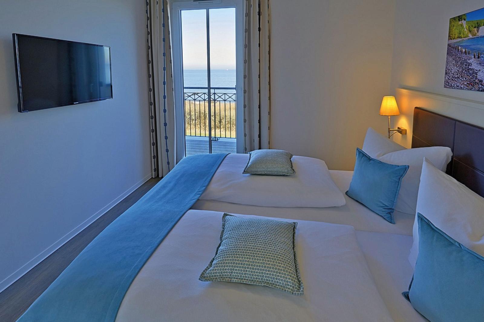 Zimmer mit Blick aufs Meer, Bett mit Kissen und TV an der Wand.