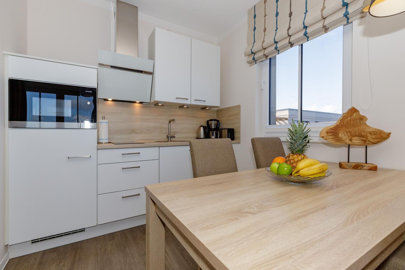Küche mit Essbereich, Fenster, Küchenschränke und Obst auf Tisch.