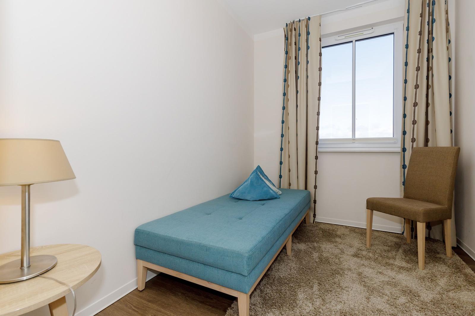 Ein Raum mit blauer Couch, Stuhl und Fenster mit Vorhängen.