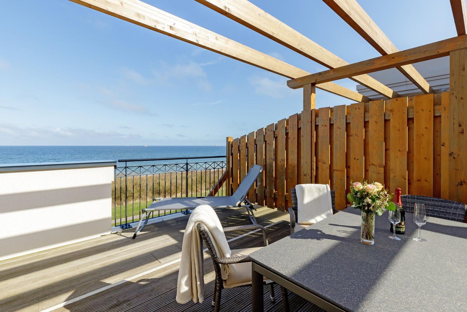 Terrasse mit Sitzgruppe und Meerblick unter Holzüberdachung.