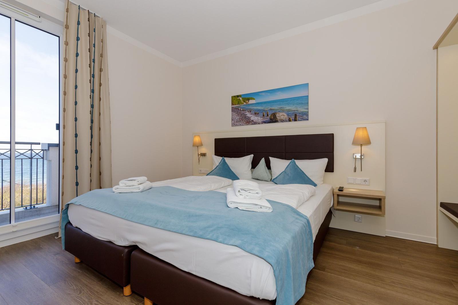 Schlafzimmer mit Bett, Balkon und Meerblick. Wandbild und Nachttische.