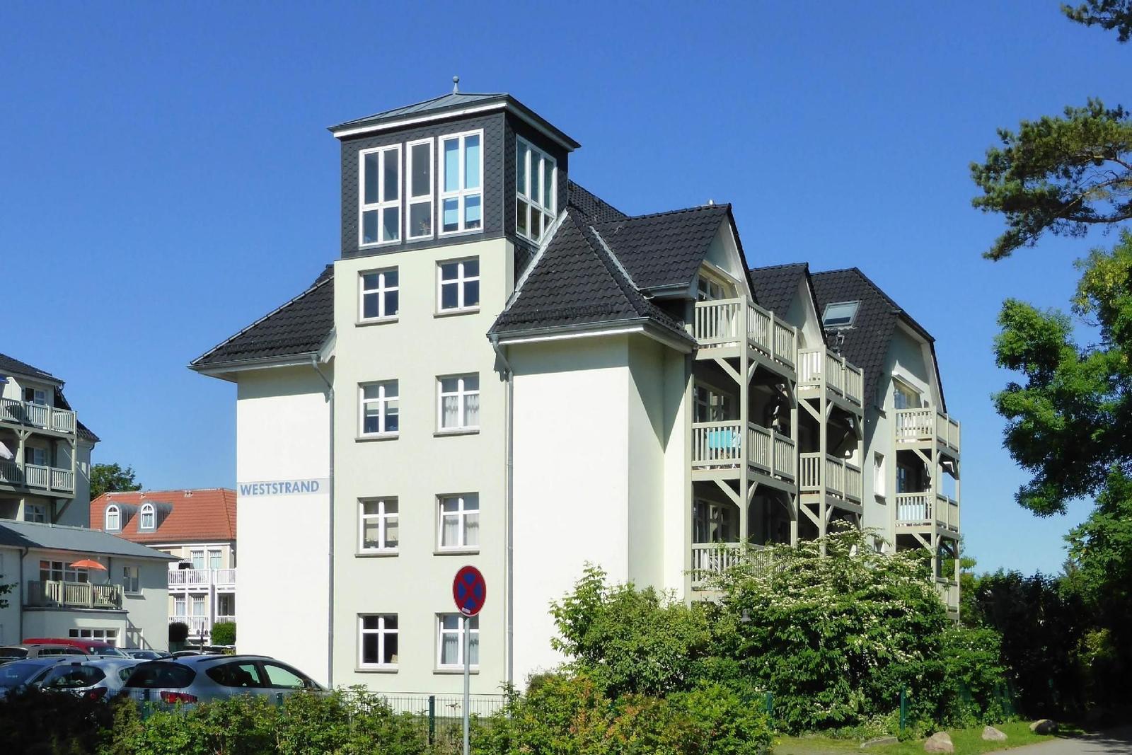 Ferienhaus mit Balkonen und Dachterrasse. An der Straße steht ein Schild mit der Aufschrift WESTSTRAND.