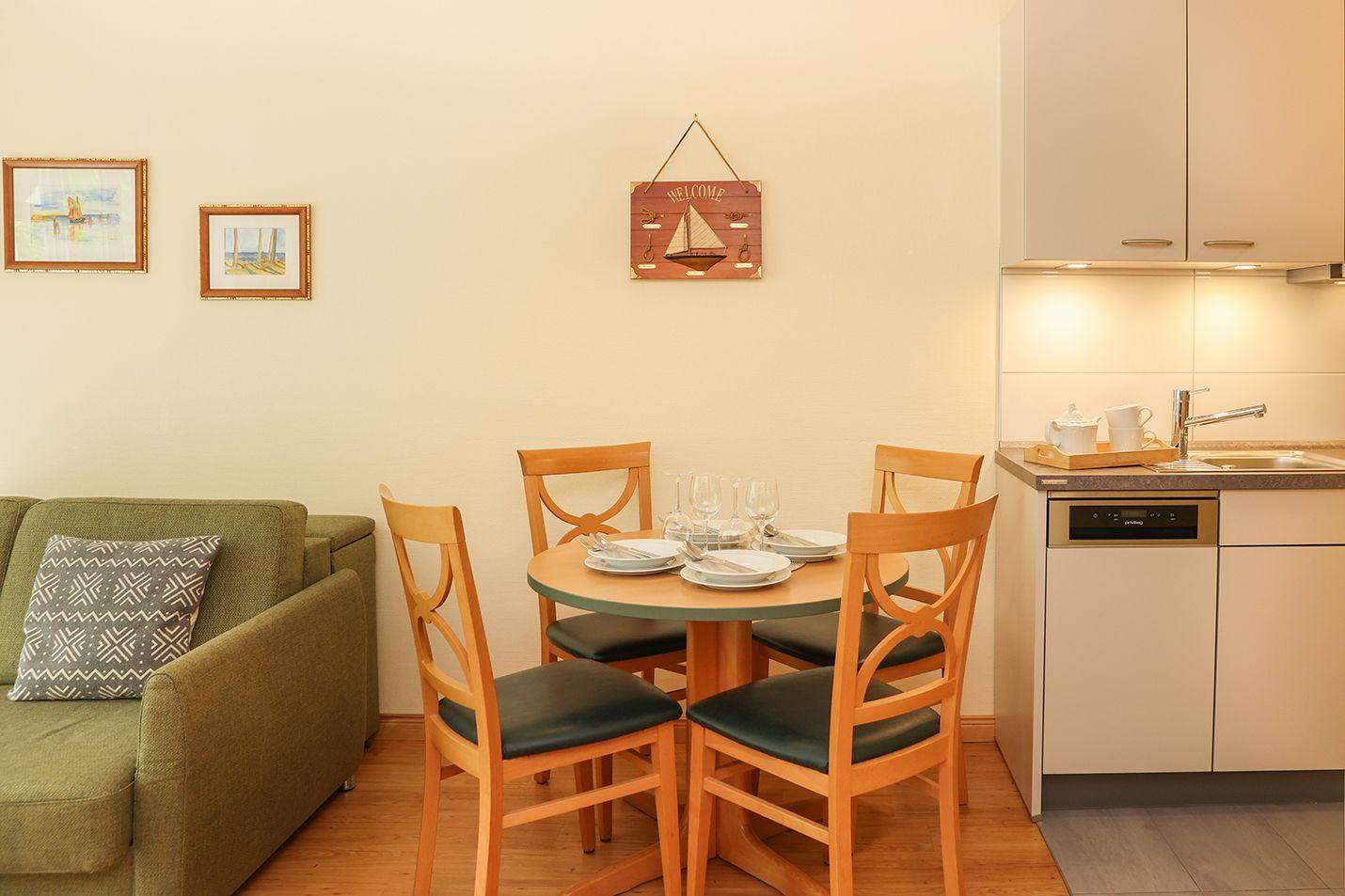 Essbereich mit runder Tisch und vier Stühlen. Küche mit Spüle und Kabinett. Sofa mit Kissen.