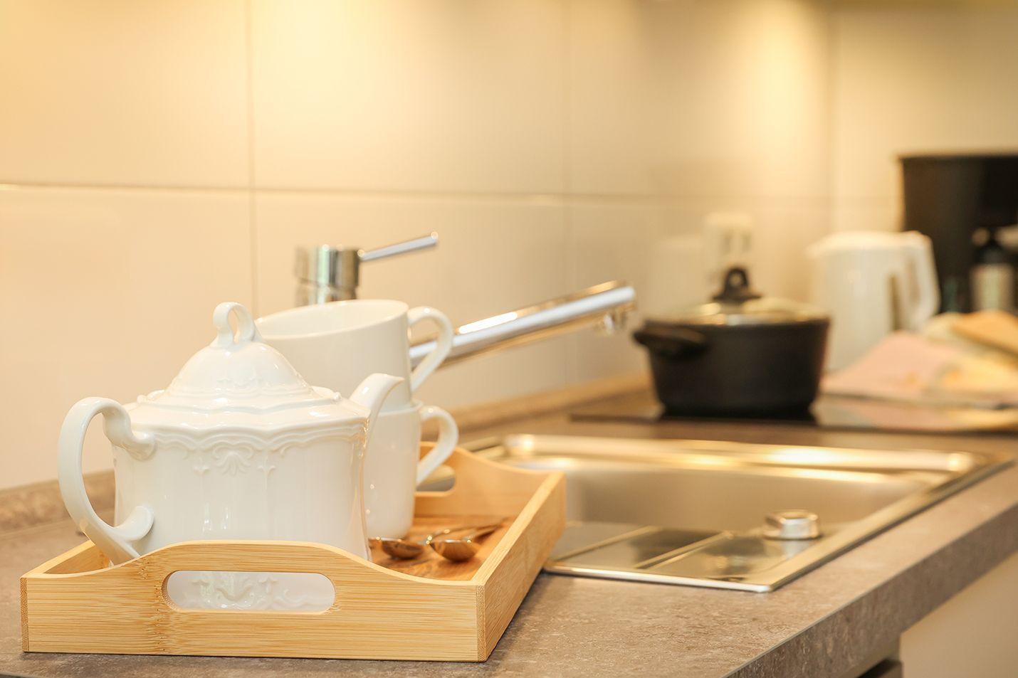 Küchenbereich mit weißer Teekanne, Tasse und Holztablett auf Arbeitsfläche.