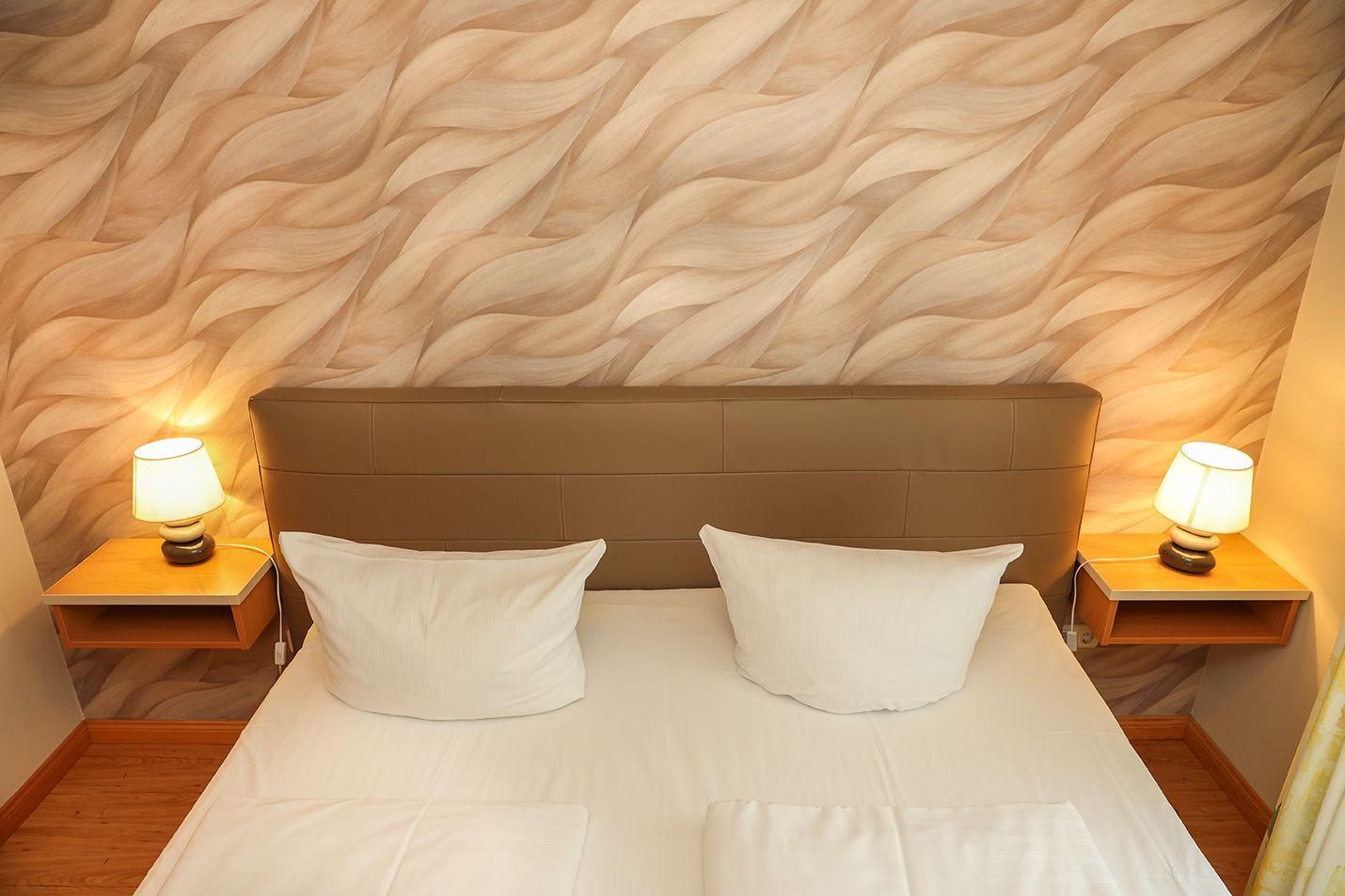 Schlafzimmer mit Bett, Kopfteil und Nachttischen mit Lampen an einer strukturierten Wand.