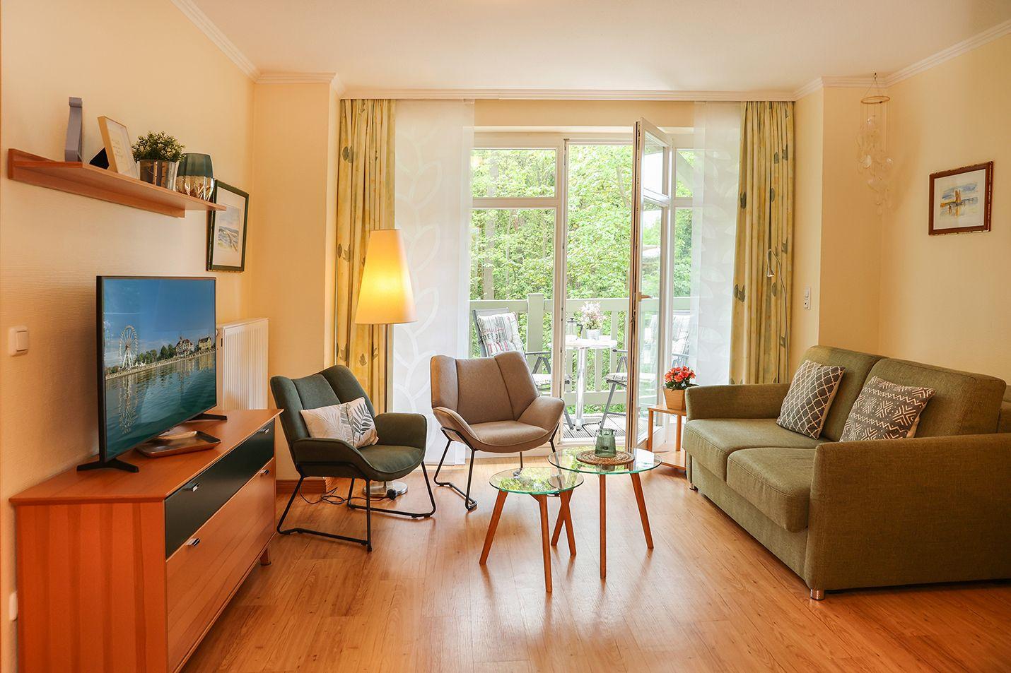 Wohnzimmer mit Sofa, zwei Sesseln, TV und Balkonansicht