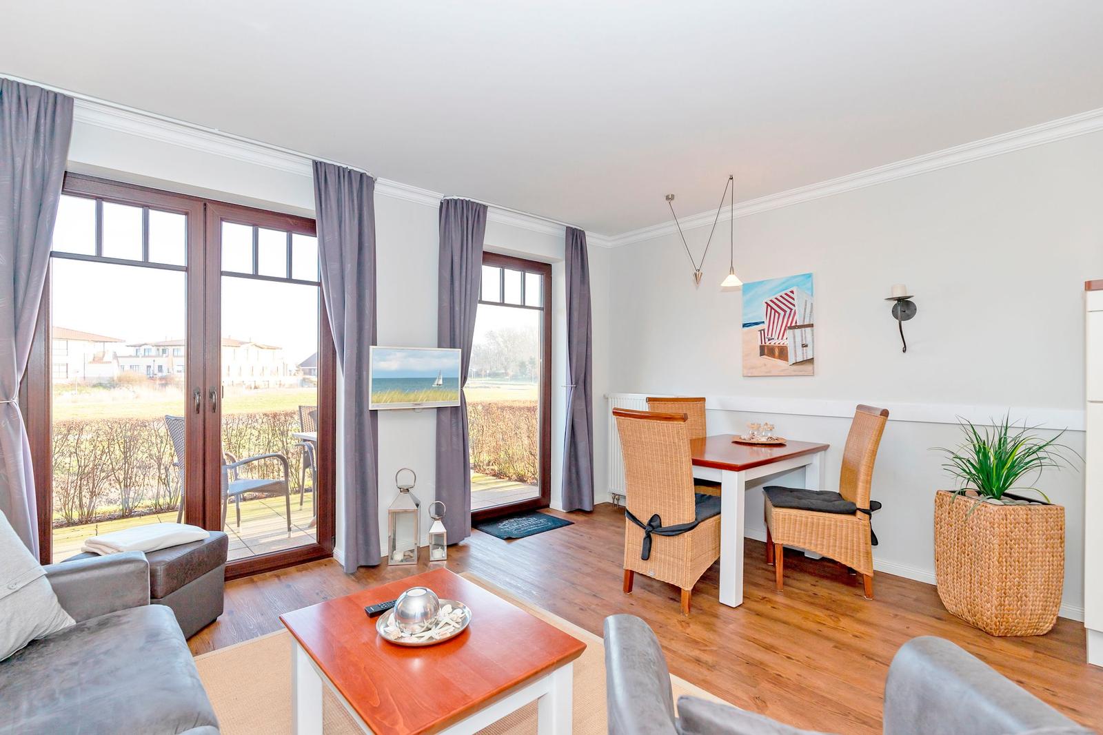 Wohn- und Essbereich mit Holzboden, großen Fenstern und einem Balkon.