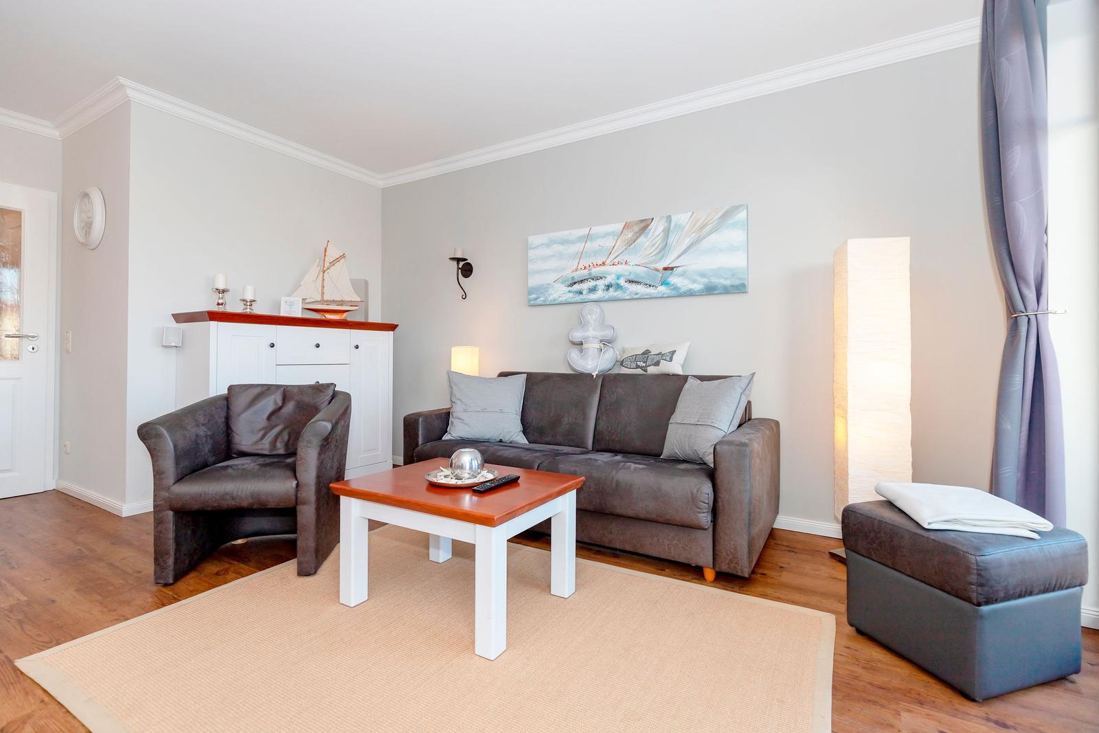 Wohnzimmer mit Sofa, Sessel, Tisch und Wandbild mit Segelboot.